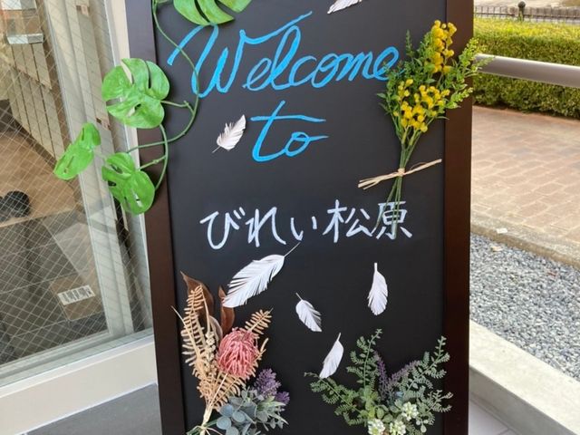 歓迎の言葉が書かれた看板 ウェルカムボード 温かい歓迎のことばが手書きされ、訪れる方々を優しく迎え入れてくれる看板です。花々と緑が添えられ、鮮やかな配色が目を引きます。