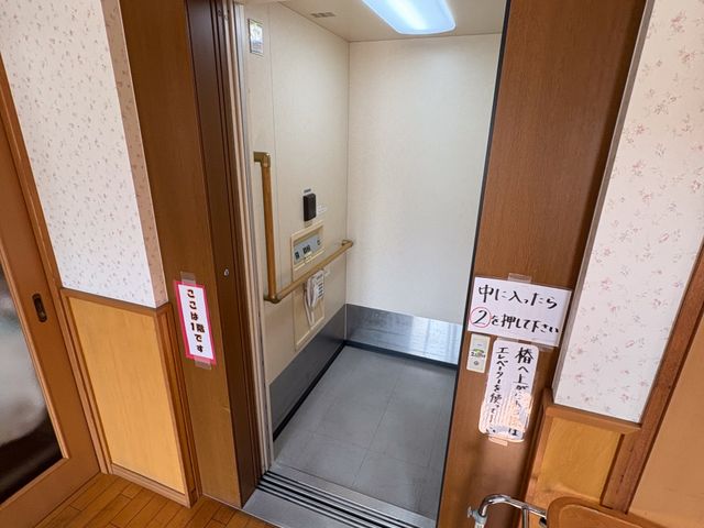 浴室前のエレベーター エレベーター   木目調のやさしい雰囲気の前に、エレベーターがあります。手すりや案内表示があり、移動しやすい工夫が感じられます。