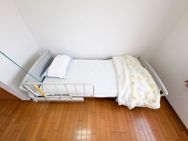 シンプルな居室のベッド 居室   木目の床にベッドが置かれた、落ち着いた一人用の居室です。掃除やベッドまわりの整えやすさが感じられます。
