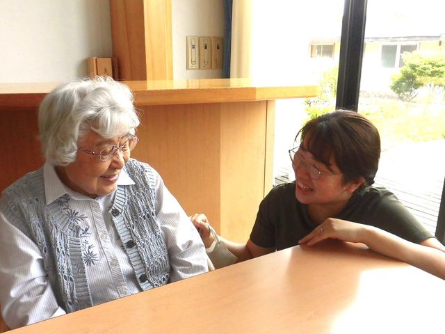 共有スペースでの優しい会話 ラウンジ 和やかな雰囲気のラウンジで、スタッフと利用者が対話を楽しむ様子です。ゆったりとした時間が流れています。