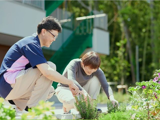 スタッフと園芸の中庭 人物 中庭での植物の手入れに取り組むスタッフの姿。温かい日差しのもと、共に作業を楽しむ姿が印象的です。