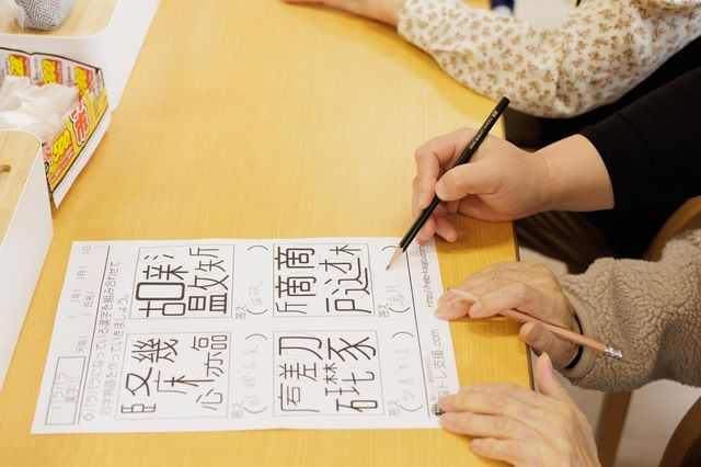 手元で文字練習中の人 多目的室 手元で行われる落ち着いた文字練習は、利用者同士の交流ができる楽しいひとときです。