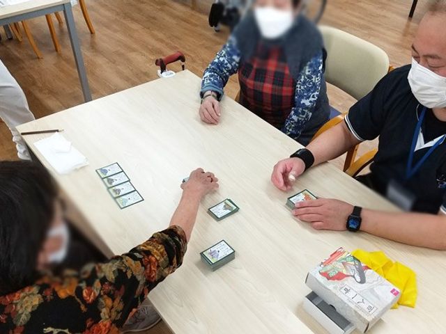 カルタで談笑する部屋 ラウンジ 自然光が差し込む広い空間で、皆で楽しくカードゲームをしています。お互いのコミュニケーションが活発です。