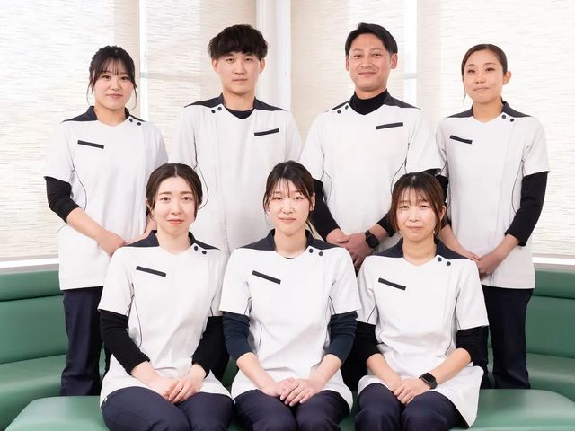 白衣のスタッフ集合 スタッフイメージ   白衣を着たスタッフの皆さんが、ソファのある明るい空間で並んでいます。落ち着いた雰囲気で、チームで支える職場を想像しやすいです。