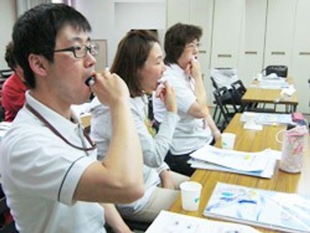 食堂で体操する職員 食堂   明るい食堂で、職員の方々が椅子に座って体操をしています。就業後の支援やレクリエーションの雰囲気が伝わる場面です。