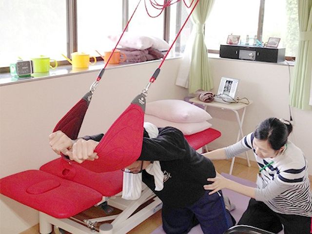機能訓練室の様子 機能訓練室 明るい室内で、サポートを受けながらリハビリに取り組む様子です。自然光が心地よい環境です。