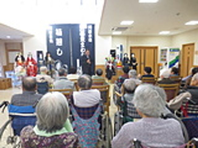 多目的室での楽しいひととき 多目的室 車椅子に座った方々が演者の歌に合わせて手拍子をして、笑顔で音楽の時間を楽しんでいます。