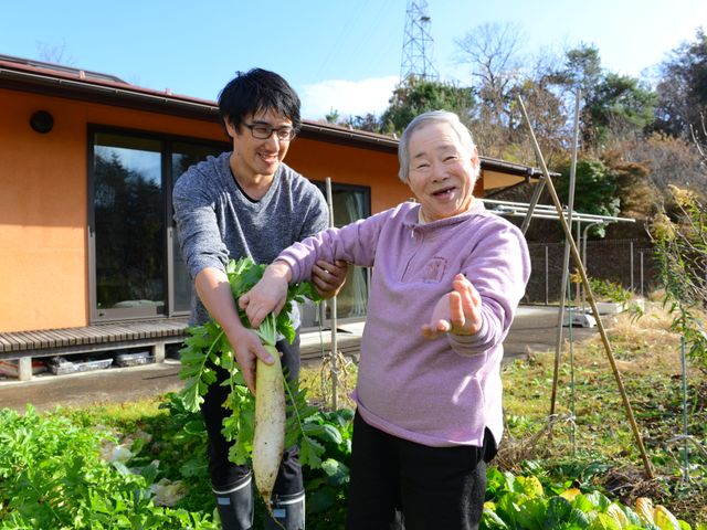 笑顔で野菜を収穫する人々 庭でスタッフとともに野菜を収穫する笑顔の明るい光景です。自然と触れ合いながら、心地よい時間を過ごすことができます。