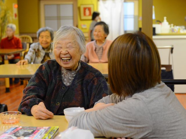 笑顔の高齢者とスタッフ 笑い声が響く明るい食堂で、スタッフが高齢者と心温まる会話を楽しんでいます。やりがいのある環境でのお仕事に興味はありませんか？