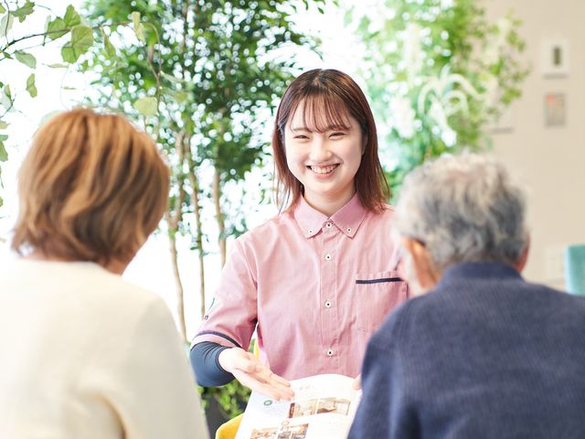 笑顔のスタッフと利用者の相談室 ラウンジ   明るい空間で、スタッフが利用者の方と笑顔で話しています。植物が多く、落ち着いて相談しやすい雰囲気です。