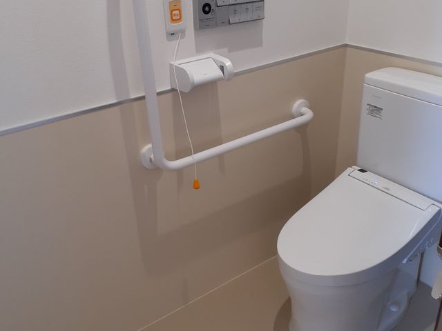 手すり付きの安全なトイレ 居室トイレ 快適さと安全性を考慮した設計のトイレです。手すりや非常呼び出しボタンがあり、利便性と緊急時の安心を提供しています。