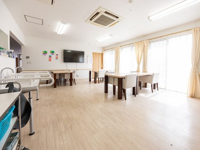 施設の明るいダイニング ダイニングルーム 広々としたダイニングルームは天井が高く、自然光がたっぷり差し込んでいます。共有の食事やコミュニケーションの場として理想的です。