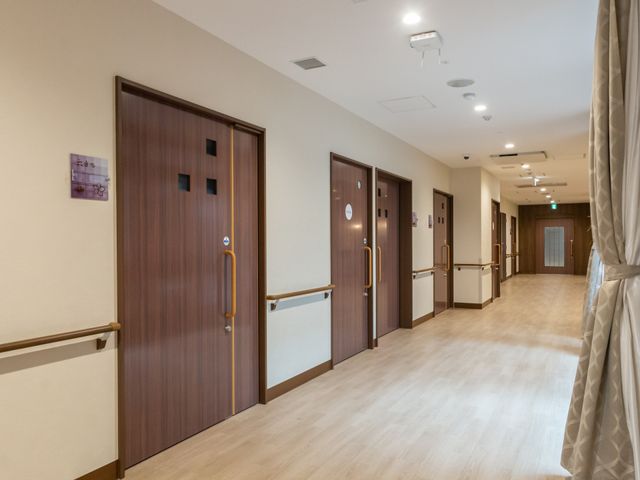 木製の扉が並ぶ廊下 廊下 広々とした廊下には手すりが設置され、移動が安心です。温かみのある木製の扉が特徴です。