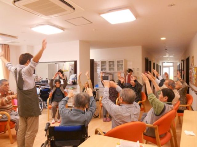 活動する人々の多目的室 レクリエーション活動 明るく広々とした室内で、利用者の方々が一緒に体操をしています。楽しみながら健康維持が図れる環境が整っています。
