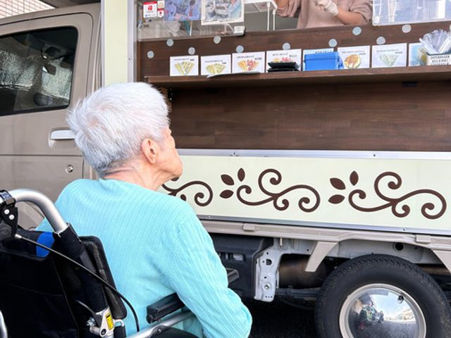 スイーツを購入する様子 エントランス 移動販売車からスイーツを購入できる楽しいひとときです。スタッフと会話も楽しまれます。