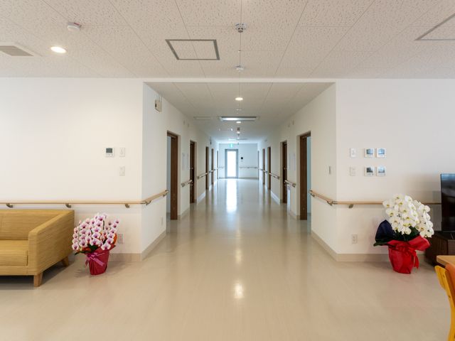 ゆったり廊下 廊下 手すり付きの広々とした明るい廊下です。壁には花の装飾があり、温かみのある雰囲気を演出しています。