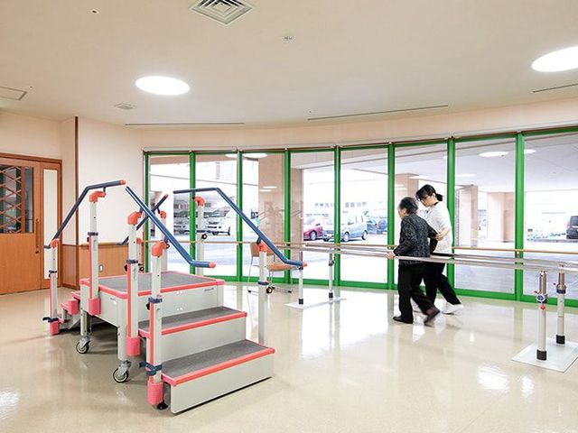 訓練用機器が並ぶ廊下 機能訓練室 訓練用の器具が整った明るい空間で、スタッフの支援を受けながら歩行の練習をしている様子です。安心してご利用いただけます。