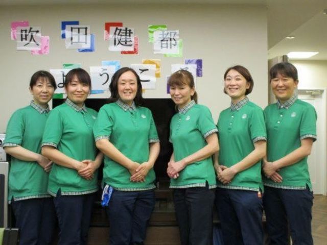 スタッフ集合の掲示前 スタッフイメージ   緑のユニフォームを着たスタッフの皆さんが、掲示の前で並んでいます。明るい雰囲気で、働く様子をイメージしやすいです。