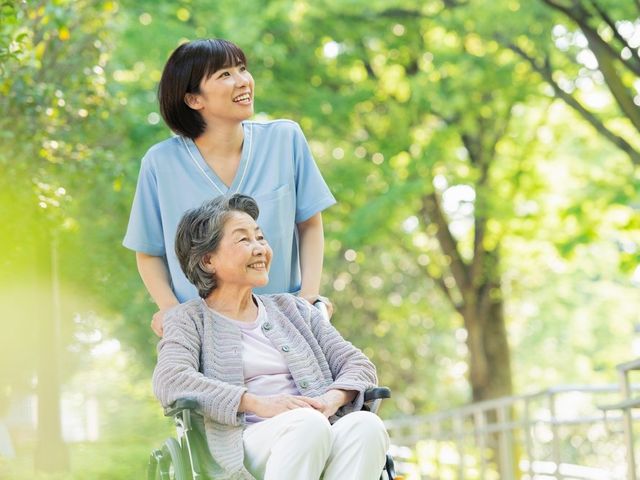笑顔の介護士と利用者が庭を楽しむ様子 庭 青空の下、介護士が利用者と共に庭を散策しています。自然豊かな空間でリラックスできる時間を提供します。