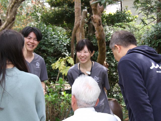 笑顔で会話する人々と中庭 中庭 緑あふれる中庭で、明るい笑顔を交わすスタッフとご利用者様の様子が伺えます。安らぎと人とのふれあいを大切にしています。