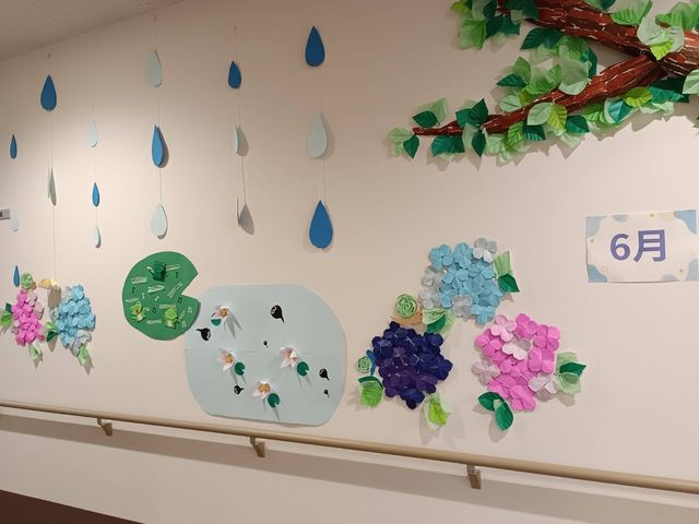 梅雨飾りの廊下 廊下   壁に季節の飾りが施された、明るい廊下です。手すりがあり、移動しやすい工夫が感じられます。