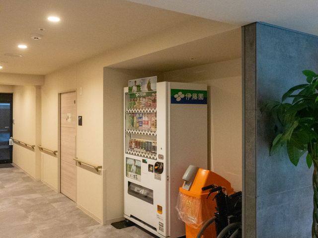 エントランス周辺の様子 エントランス ゆとりあるエントランスには、観葉植物が飾られ、優しい雰囲気を醸し出しています。安心してご利用いただけるよう、手すりや自動販売機も設置されています。
