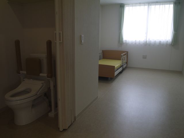快適な居室 居室 手すり付きのトイレとシンプルなベッドが配置された居室です。明るい窓からは自然光が差し込み、穏やかな時間をお過ごしいただけます。
