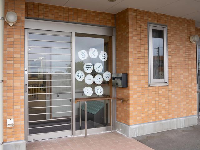 さくらデイサービス入口 エントランス   レンガ調の外壁に、ガラス扉の入口が設けられています。手すりもあり、出入りしやすい印象です。