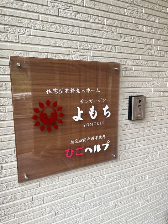 外壁に設置されたブラウンのプレートにはホーム名と併設の訪問介護ステーションの名前が書かれている。