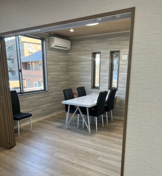 4人掛けのテーブルが置かれている部屋にはエアコンがあり、窓のそばにはもう一脚いすが置かれている。