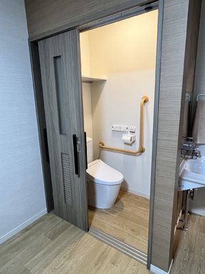 スライド式のドアが設置されたトイレにはエル字型の手すりが付き、外には洗面所もある。