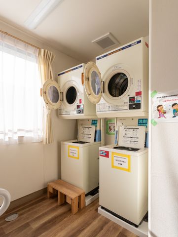 洗濯機が並ぶコインランドリー コインランドリー 明るい日差しが差し込む清潔なランドリールームです。洗濯機がサイドバイサイドで設置されています。