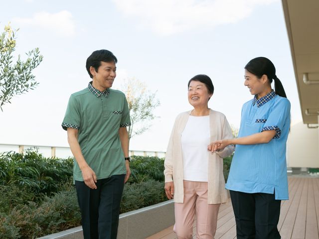 屋外テラスで会話する様子 テラス   明るい屋外テラスで、利用者の方とスタッフが笑顔で会話しています。開放感のある空間で、自然に声をかけやすい雰囲気です。
