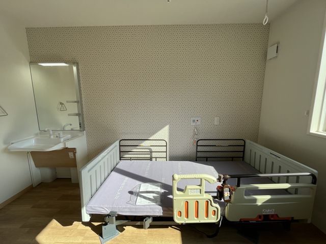 ベッドと洗面台の居室 居室 明るい光が差し込む快適な居室です。調整可能なベッドが設置されており、安心して過ごせます。