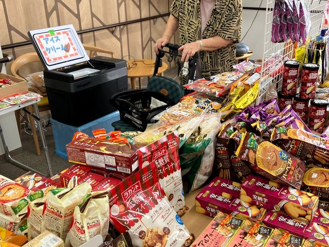 お菓子販売会のリビング リビング お菓子が並ぶ明るいリビングです。利用者の方が買い物を楽しめる、にぎやかな雰囲気が伝わります。
