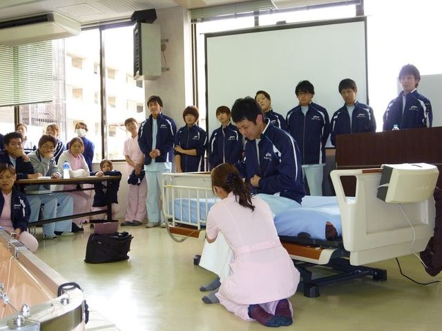 介護研修の様子 機能訓練室 実践的なケア技術を学ぶ研修風景です。専門スタッフによる説明を真剣に聞く姿が伺えます。