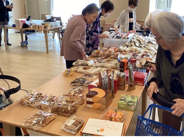 楽しい交流の場 ラウンジ 多様なお菓子が並ぶテーブルで入居者同士が会話を楽しんでいます。活気に満ちた雰囲気です。