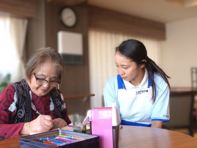 介護士とのアクティビティ リビング 広々としたリビングで、介護士が利用者と一緒にアクティビティを楽しんでいます。自然光が心地よい空間です。