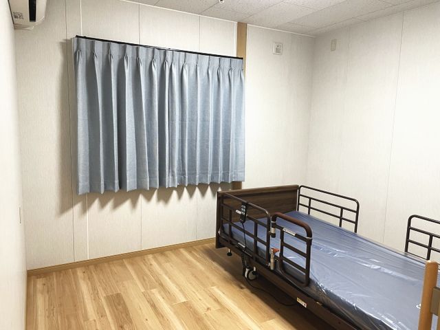 明るい個室の居室 居室 ベッドとカーテンのシンプルな空間で、落ち着いた雰囲気が広がっています。