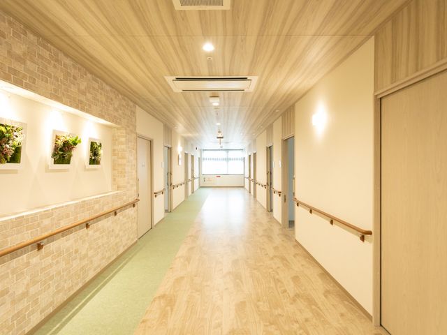 木目調の明るい廊下 廊下 明るい廊下は、木目調の床と壁に包まれ、心地よい空間を提供します。手すりが設置され、安全に配慮されています。
