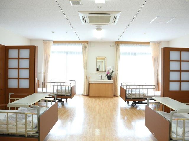 明るい床の共有スペース 居室 床が明るい木目調で統一された広々とした共用ラウンジです。周囲には植物が飾られ、安心してくつろげる空間が広がっています。