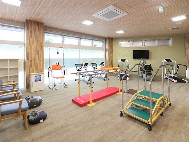 機能訓練室の運動器具 機能訓練室   明るい窓辺に、運動器具や手すりがゆったり配置されています。歩行練習や体を動かす場として使いやすそうです。