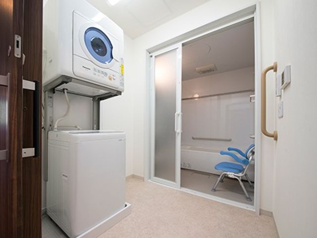 洗濯機と浴室のある洗濯室 コインランドリー   洗濯機と乾燥機が備わった、使い勝手のよい洗濯スペースです。浴室へつながる出入口もあり、動線が分かりやすく整っています。