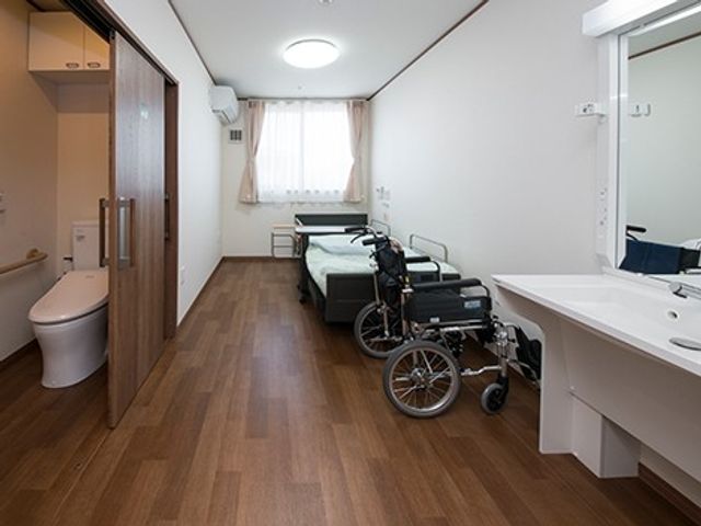 車いすのある居室 居室   窓から自然光が入る落ち着いた居室です。車いすやベッド、洗面台があり、日常の動きを支えやすい環境です。