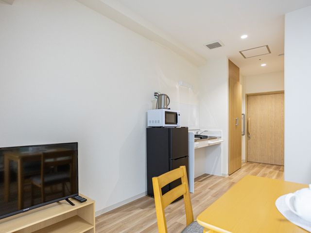 居室の一角 居室   明るい居室の一角に、テレビや冷蔵庫、電子レンジが整っています。木目調の床で、落ち着いて過ごしやすい雰囲気です。