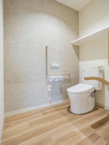 手すり付きトイレ トイレ   手すりと広めの空間があり、移動しやすそうなトイレです。明るい木目調の床で、落ち着いた雰囲気になっています。