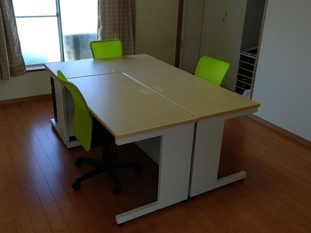 明るい部屋と机と椅子 多目的室 自然光が降り注ぐ明るい部屋に、広々とした机と快適な椅子が整えられています。