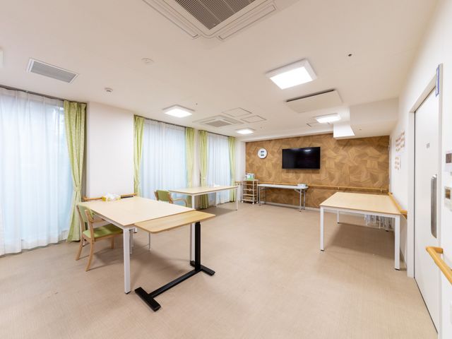 明るい食堂のような空間 ダイニングルーム   大きな窓から光が入り、ゆったりとしたテーブル配置で動きやすい空間です。壁面のテレビもあり、食事や会話の時間を過ごしやすそうです。