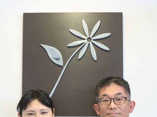 スタッフ2人と花の壁飾りの前  