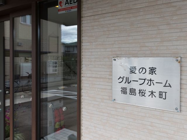 白壁に看板のある入口 玄関 温かみのあるエントランスで、来訪者を迎える準備が整っています。訪れる方々がすぐに安心感を覚えるデザインです。